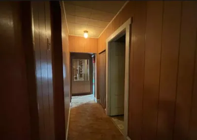 Dim hallway with wood paneled walls, drop ceiling, and worn carpet leading to a back room.