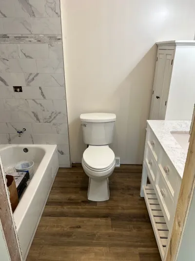 A bathroom mid-renovation with a marble-tiled tub surround, new toilet, and vanity awaiting hardware.