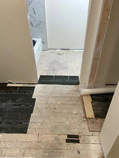 Bathroom renovation in progress showing subfloor demolition and tile work visible through an open doorway.