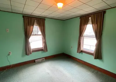 Empty room with green walls, worn carpet, dark wood trim, and a drop ceiling before renovation.