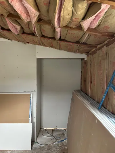 Construction in progress showing hung drywall and exposed pink fiberglass insulation along a sloped ceiling.