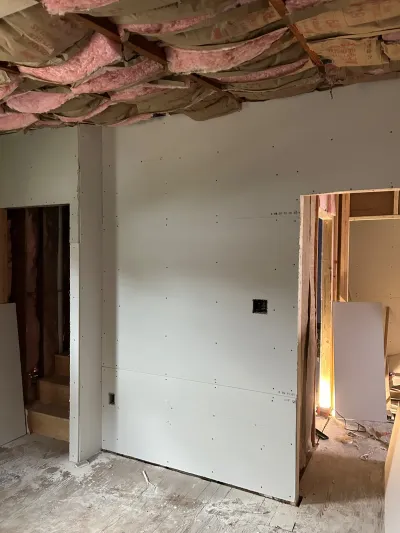 Basement under construction with hung drywall, exposed ceiling insulation, and a framed doorway.