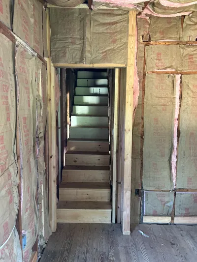 Unfinished stairwell with exposed insulation and stud walls leading to a narrow staircase.