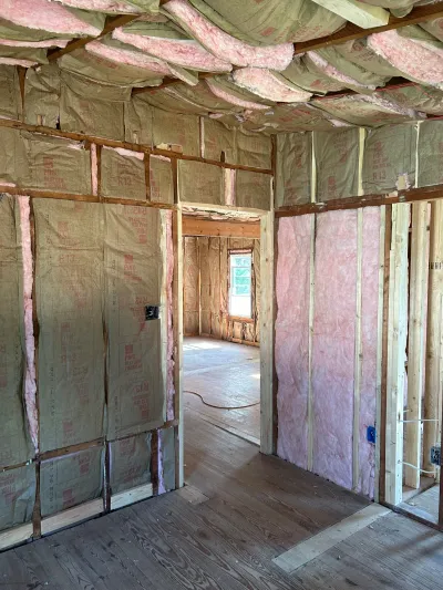 Unfinished room with exposed wood framing, pink fiberglass insulation, and a doorway leading to another room.