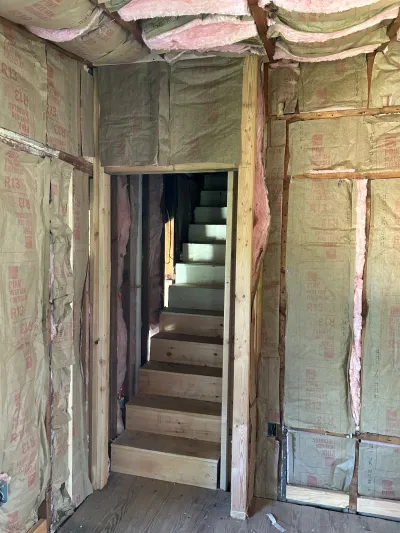 Unfinished stairwell with exposed insulation and a bare wood staircase during a home renovation.