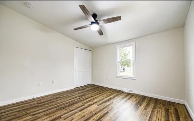 Empty bedroom with vaulted ceiling, wood-look plank flooring, and a bifold closet door.