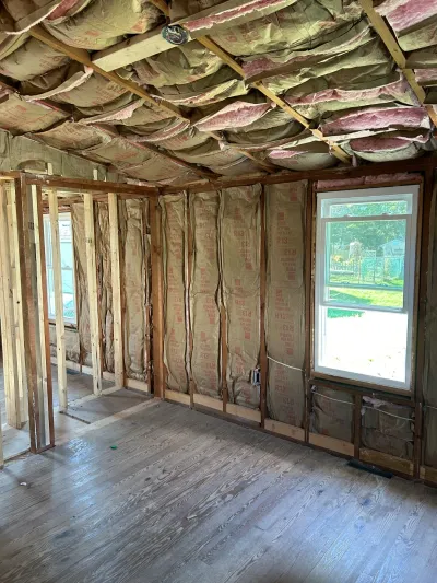 Room mid-renovation with exposed wall and ceiling framing, insulation batts, and a window overlooking the yard.