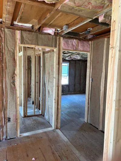 Framed-out interior under construction with exposed studs, ceiling joists, and insulation batts.