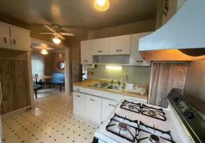 A dated kitchen with white laminate cabinets, wood paneling, and a gas range, seen from before renovation.