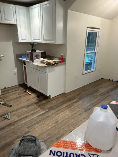 A kitchen mid-renovation with white cabinets installed, new plank flooring, and tools scattered about.