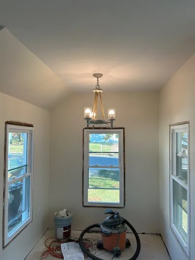 A sunroom under renovation with a vaulted ceiling, chandelier, and exposed subfloor with tools.