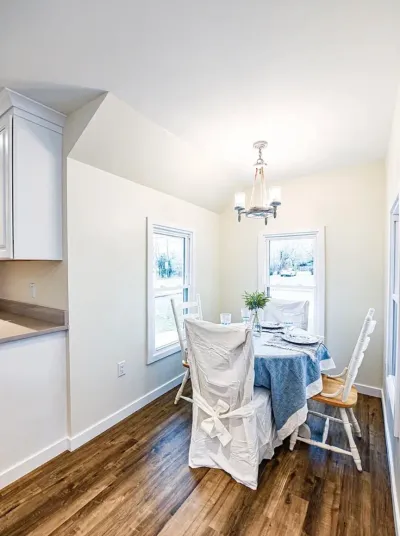 Bright dining nook with vaulted ceiling, pendant light, wood floors, and a table set for a meal.
