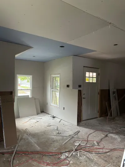 A kitchen mid-renovation with taped drywall, exposed subfloor, and construction debris scattered across the floor.