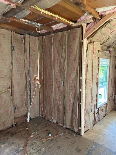 Construction interior showing exposed wall studs with pink insulation, rough electrical wiring, and a new window.