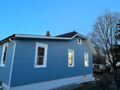 Side view of a house with new blue siding and white trim, photographed at dusk with a work van parked nearby.
