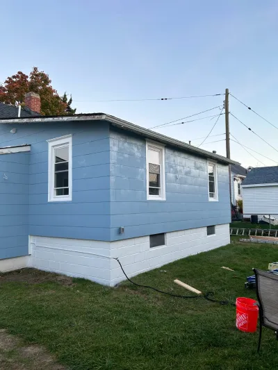 Side view of a house with weathered blue siding and a white foundation, before exterior renovation work.