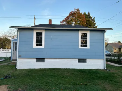 Side view of a house with new blue siding, white trim, and a painted concrete block foundation.