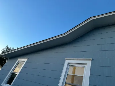 Close-up of a house exterior with blue-grey siding and a distinctive curved roofline against a clear sky.