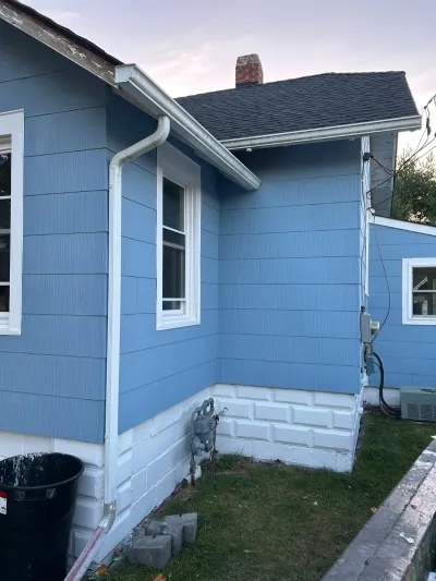 Corner of a house with new blue siding, white trim, gutters, and a painted foundation.