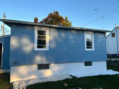 Side view of a house with new blue lap siding and a painted white block foundation.