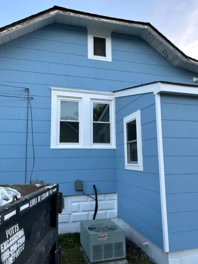 Newly sided blue house exterior with white trim, windows, and an outdoor HVAC unit near the foundation.