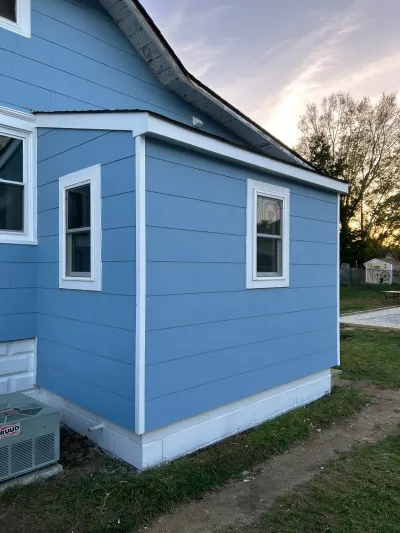 Blue fiber cement siding addition with white trim and two windows, photographed at sunset.