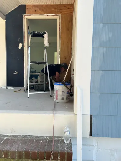 A worker installs trim near a doorway on a home mid-renovation, with new blue siding partly installed.