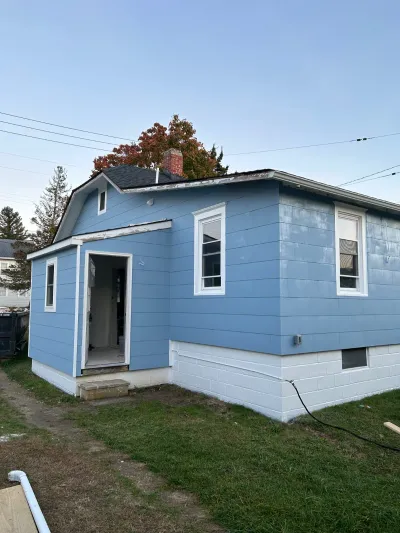 Side view of a house with new blue siding, white trim, and an open door leading into an unfinished addition.