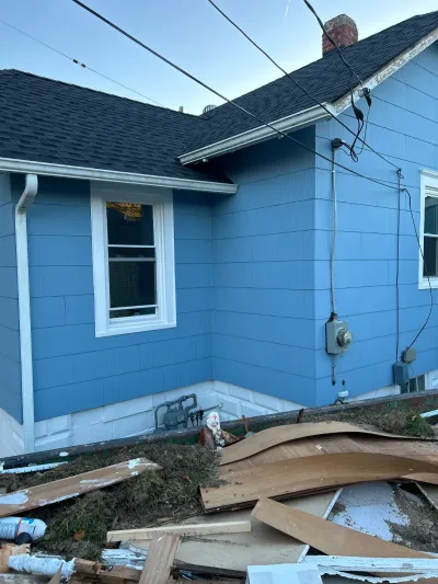 Corner of a house with new blue siding and white trim, with construction debris piled in the foreground.