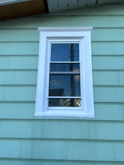 Close-up of a white-trimmed double-hung window on a house with seafoam green lap siding.