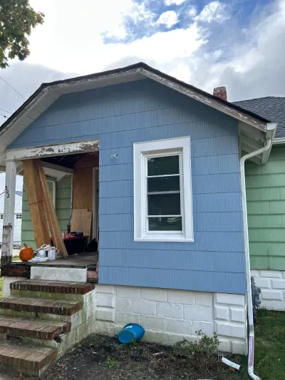 Home exterior mid-renovation with new blue siding, a fresh window, and an open porch under repair.