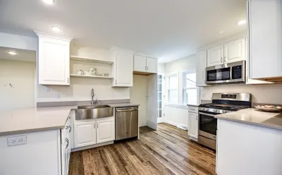 Renovated white kitchen with farmhouse sink, stainless appliances, and wood-look plank flooring.