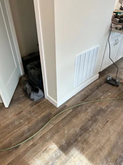 Freshly installed wood-look plank flooring with a pneumatic nailer and air hose during an in-progress renovation.