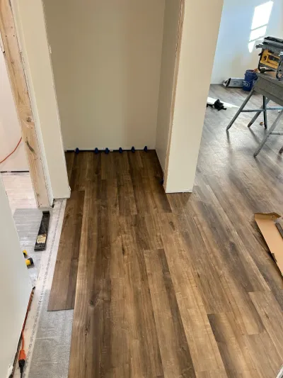 Vinyl plank flooring being installed in a hallway closet with spacers and tools staged nearby.