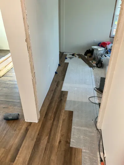 Hallway mid-renovation with dark vinyl plank flooring partially installed over exposed underlayment.