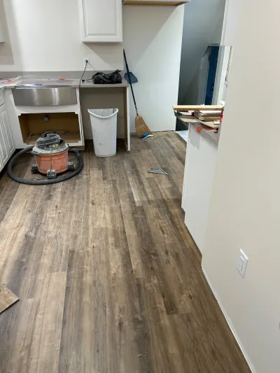 Kitchen mid-renovation with new plank flooring, white cabinets, and a farmhouse sink covered in plastic.
