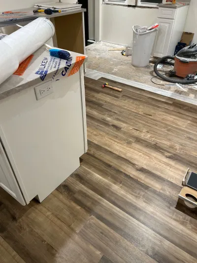 Kitchen renovation in progress with new wood-look vinyl plank flooring being installed over bare subfloor.
