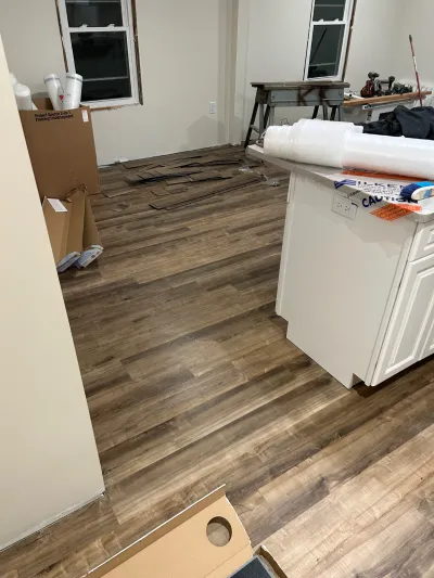 A kitchen mid-renovation with new plank flooring partially installed and construction materials scattered about.