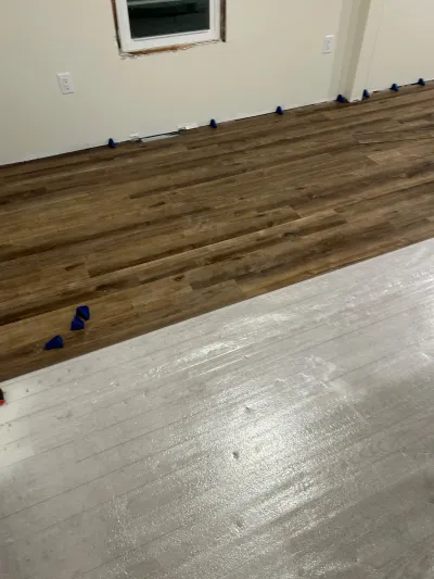 Vinyl plank flooring being installed with spacers along the wall, showing a transition between two plank colors.