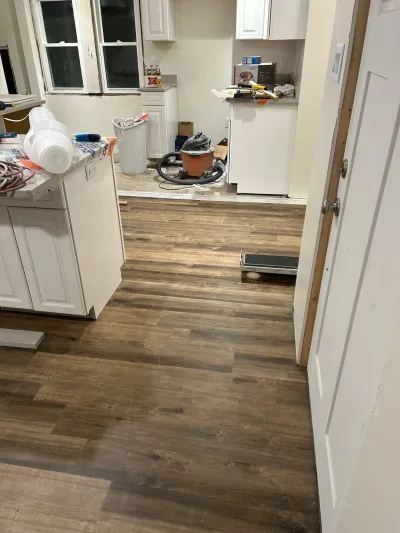 A kitchen mid-renovation with new wood-look plank flooring, white cabinets, and scattered tools.