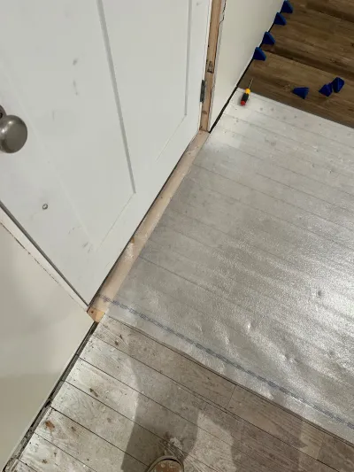 Flooring underlayment and subfloor visible at a doorway during a mid-renovation flooring installation.