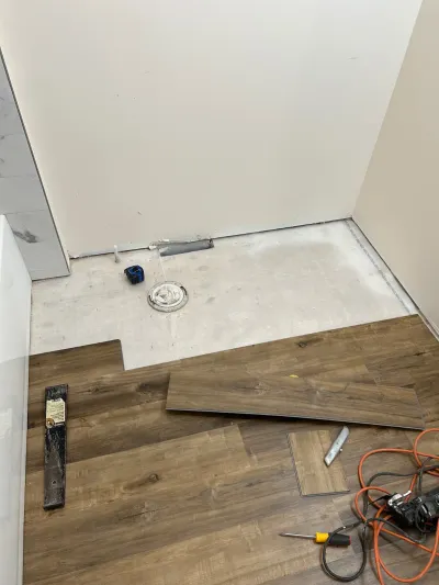Vinyl plank flooring installation in progress in a bathroom, with tools scattered on the finished section.