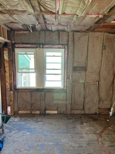 Room under renovation with exposed wall studs, ceiling joists, and insulation around a window.