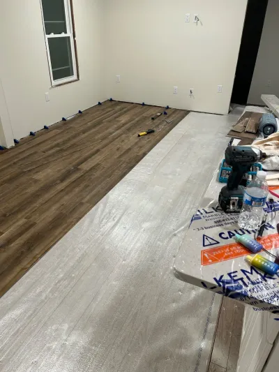 A room mid-renovation with vinyl plank flooring partially installed over underlayment and tools scattered nearby.