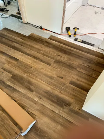 Dark walnut LVP flooring being installed with tools and materials scattered across the work area.