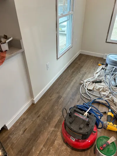 A room mid-renovation with new wood-look flooring, fresh paint, and tools scattered on the floor.