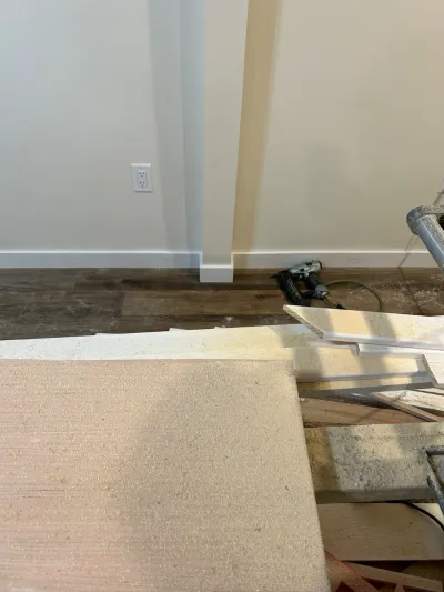Baseboard trim installation in progress with a nail gun and cut trim boards on a dusty floor.