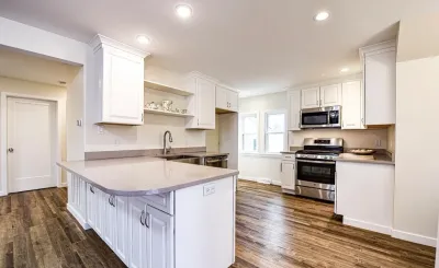 Bright white kitchen with quartz peninsula, stainless appliances, and wood-look vinyl flooring.