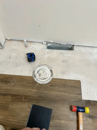 Bathroom floor mid-renovation with new wood-look vinyl plank flooring being installed around a toilet flange.