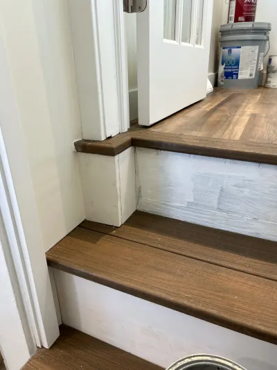 Close-up of stair treads mid-installation with new wood-look flooring and unfinished white risers near a doorway.